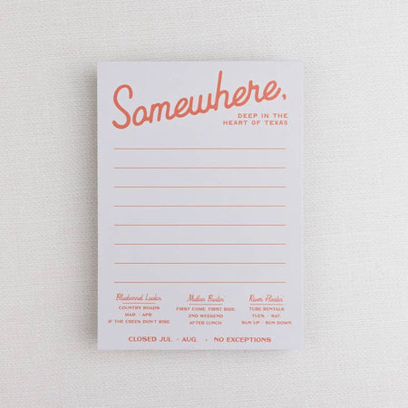 White lined notepad with orange text saying, “Somewhere, Deep in the Heart of Texas”. Various Texas places and activities listed on front of notepad.