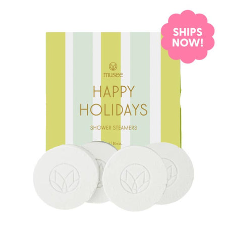 White soap discs wrapped in a lime green and mint green striped box with gold foil text saying, ,”Happy Holidays Shower Steamers”.