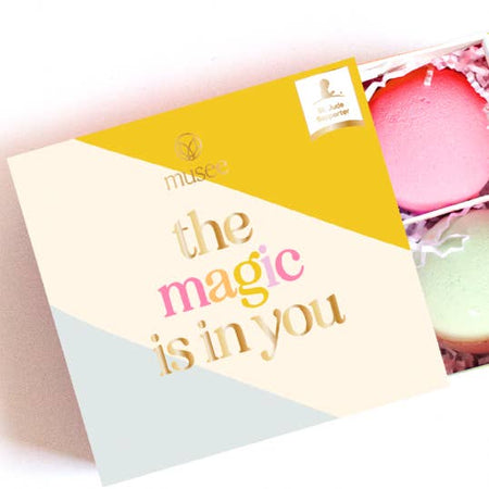 Pink and mint green soap balls wrapped in a yellow, white and blue diagonal striped box with gold foil  text saying, “The Magic is in You”.