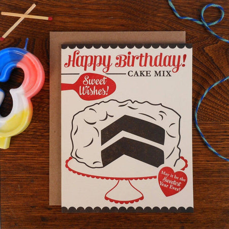 White card in the image of a vintage boxed cake mix. Red and black text saying, “Happy Birthday Cake Mix Sweet Wishes May It Be Your Sweetest Year Ever”. Image of a chocolate cake with white frosting in center of card. A brown kraft paper envelope is included.