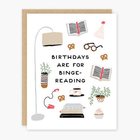White card with various birthday and book images such as open books, a reading lamp, potted plants, a birthday hat, cupcake, cup of tea and pretzels. Black text saying, “Birthdays Are For Binge-Reading”. A matching envelope is included.