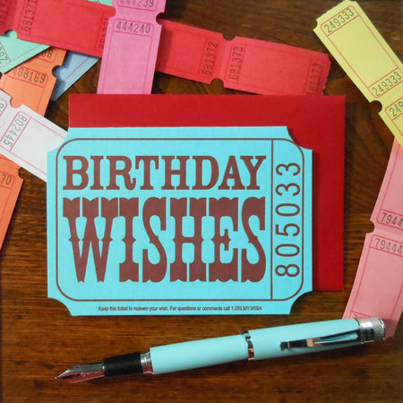 Blue card in the image of a carnival ticket with brown text saying, “Birthday Wishes”. Numbers in brown text on the side reading, “805033”. A red envelope is included.