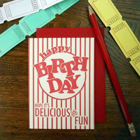 White card in the image of a circus popcorn box with red vertical stripes and red text saying, “Happy Birthday Hope It’s Delicious and Fun”. A red envelope is included.