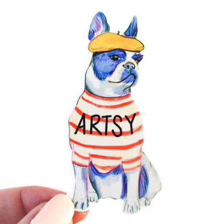 Sticker in the image of a Boston Terrier dog wearing a striped tshirt and a tan beret. Black text on the tshirt saying, “Artsy”.