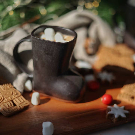 Black mug in the shape and image of a black Santa boot with handle on the left side. 