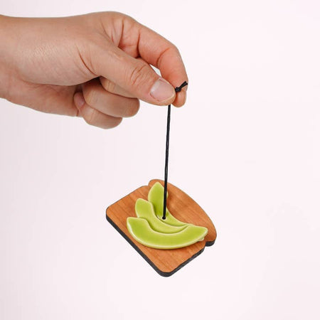 Black string ornament in the image of a wooden piece of toast with slices of green avocado on it. 