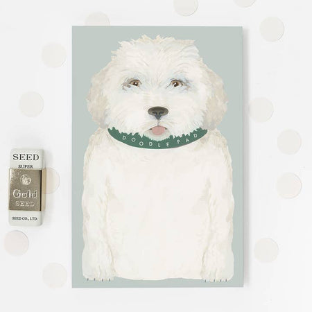 Light blue notepad with image of a white labradoodle dog wearing a green collar. White text on collar saying, “Doodle Pad”.