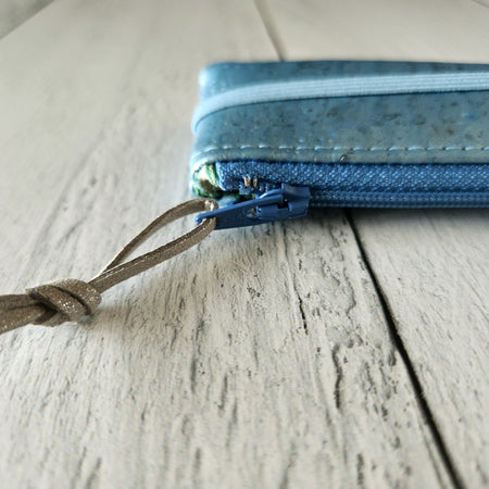 Cork rectangle pencil case in light blue color with blue zipper and light blue banding along the bottom center. Brown twine loop attached to zipper.