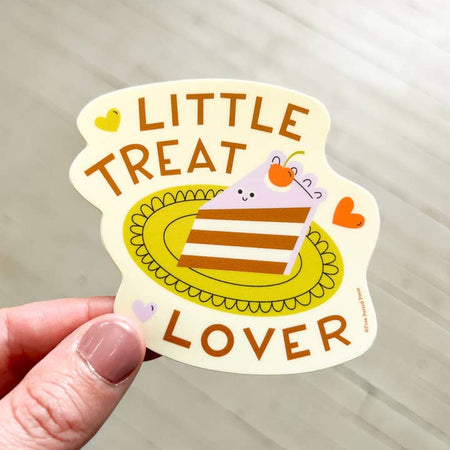 Ivory sticker with image of a slice of chocolate cake with purple frosting. Brown text saying, “Little Treat Lover”.