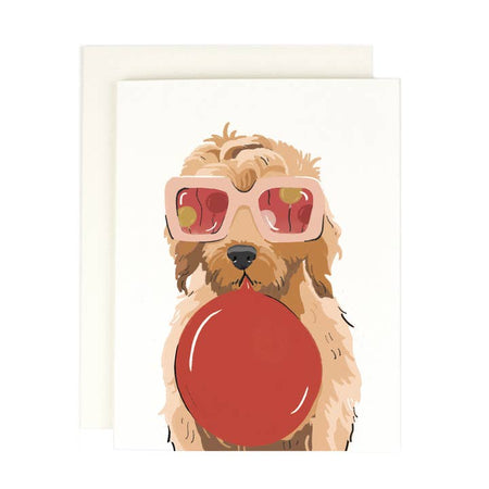 White card with image of a brown dog wearing pink sunglasses and hold a red balloon in its mouth. A white envelope is included.