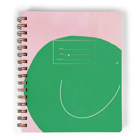 Pink notebook with large green smiley face in center of cover. Gold coil binding on left side.