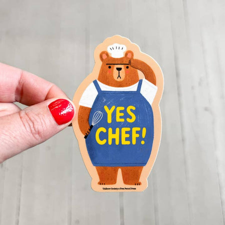 Sticker in the image of a brown bear wearing a blue apron and white chef hat holding a wire whisk. Yellow text saying, “Yes Chef!”