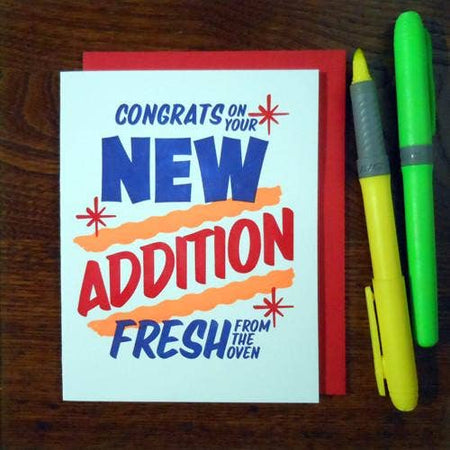 White card with red and blue text saying, “Congrats On Your New Addition Fresh From the Oven.” Text designed to look like a grocery store special sale sign. A red envelope is included.