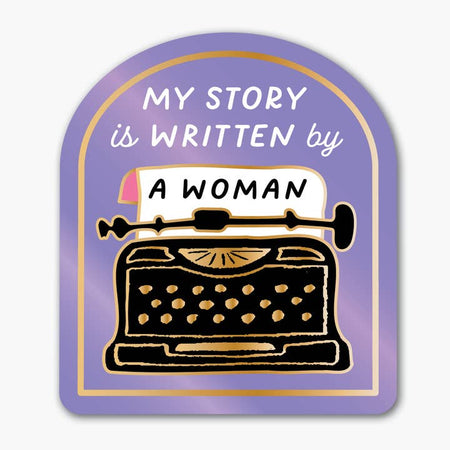 Purple sticker with image of a black vintage typewriter. White text saying, “My Story is Written by A Woman”.