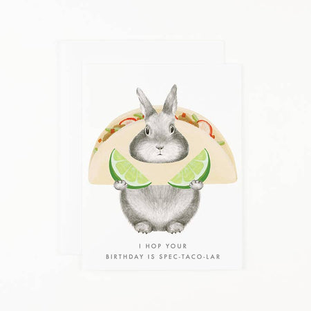 White card with image of a gray bunny holding a taco and two green limes. Gray text saying, “I Hop Your Birthday is SPEC-TACO-LAR”. A white envelope is included.