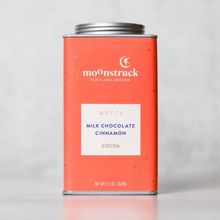 Orange tin with silver lid. White text saying, “Moonstruck” with image of a person standing on a half moon. White box in center with blue text saying, “Nutty Milk Chocolate Cinnamon Cocoa”.