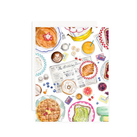 White card with images of brunch foods and a newspaper. Black text on newspaper saying, “The Birthday Times”. Foods include: pancakes, waffles, avocado toast, banana, orange juice and coffee. A white envelope is included.