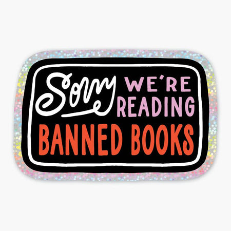 Black sticker with glitter border with white, pink and red text saying, “Sorry We’re Reading Banned Books”.