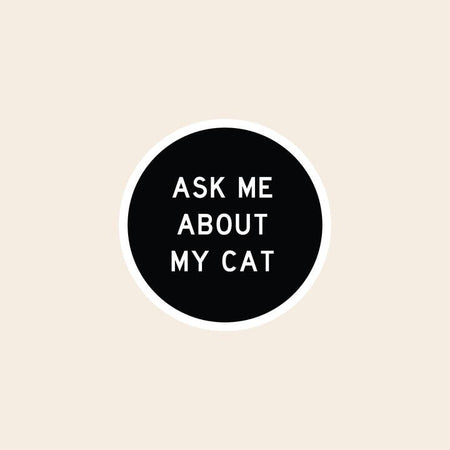 Black circular sticker with white text saying, “Ask Me About My Cat”.