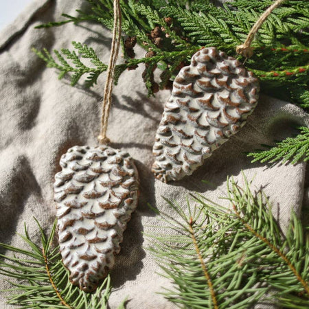 Stoneware ornament in the shape and image of a pinecone with a whitewash over the top.