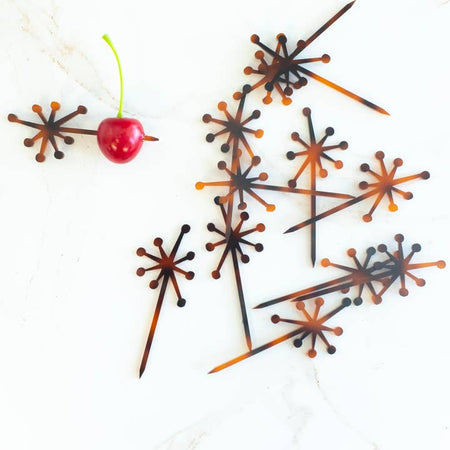 Tortoise shell brown cocktail picks in the image of a starburst design on the top and straight pointed pick on the bottom.