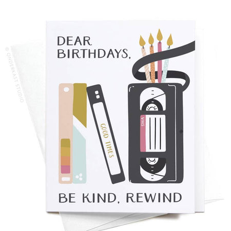 White card with black text saying, “Dear Birthdays, Be Kind, Rewind”. Images of a vintage black VCR tape with birthday candles coming out the top. Other tapes lined up vertically beside it. A white envelope is included.