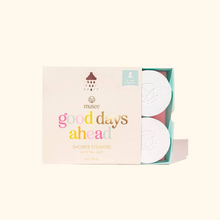 White soap discs wrapped in a pink box with rainbow text saying, “Good Days Ahead Shower Steamers”.