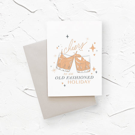 White card with gray and brown text saying, “Cheers to an Old Fashioned Holiday”. Image of two glasses with a traditional old fashioned alcoholic drink. A gray envelope is included.