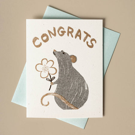 Ivory card with gold foil text saying, “Congrats”. Image of a gray ray holding a white flower. A matching envelope is included.