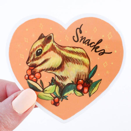 Sticker in the image of a pink heart with a chipmunk eating berries inside with black text saying, “Snacks”.