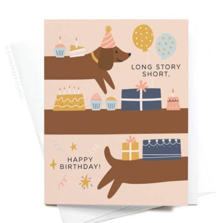 Pink card with black text saying, “Long Story Short, Happy Birthday”. Image of a brown weiner dog stretched out with birthday presents, cupcakes, and balloons on its back. A white envelope is included.