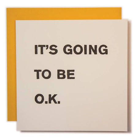 Tiny white square with black text saying, “It’s Going to Be O.K.”  A yellow tiny envelope is included.