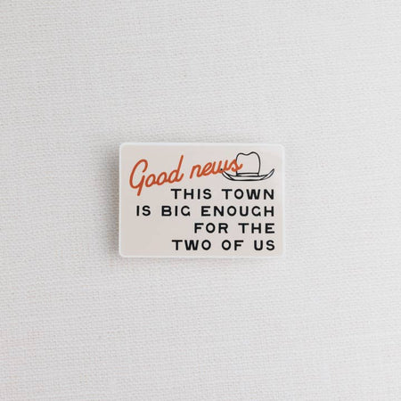 Ivory sticker with image of an outline of a cowboy hat with red and black text saying, “Good News This Town is Big Enough for the Two of Us”.