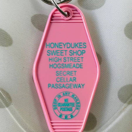 Pink vintage style motel key fob with teal text featuring the Hogsmeade sweet shop that Hogwarts students frequent.