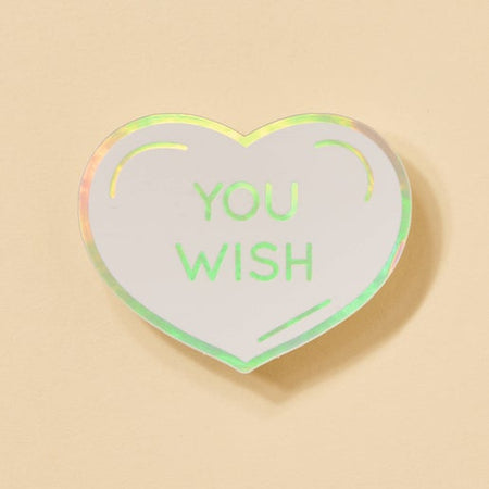 Sticker in the image of a white heart with holographic colored outline and text saying, “You Wish”.