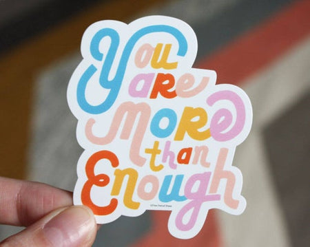 White sticker with rainbow text saying, “You Are More Than Enough”.